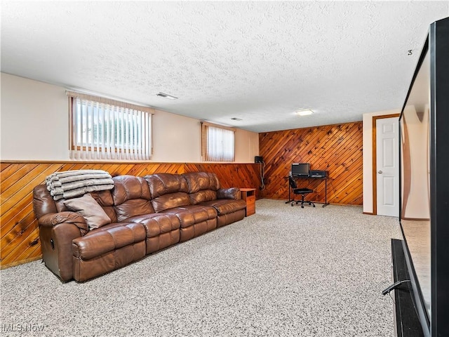 living area featuring a textured ceiling, wooden walls, carpet, visible vents, and wainscoting