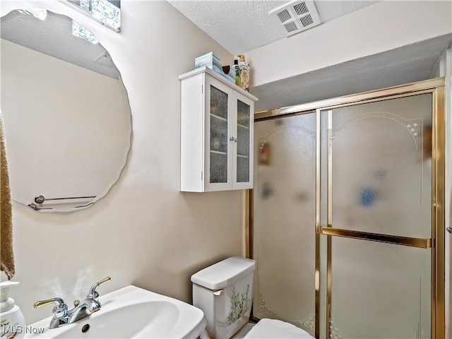 bathroom with visible vents, a stall shower, a sink, a textured ceiling, and toilet