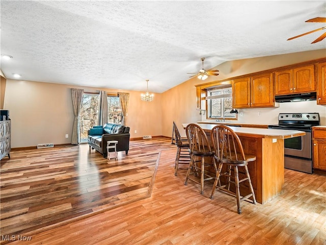 kitchen with electric range, brown cabinets, visible vents, under cabinet range hood, and a breakfast bar area