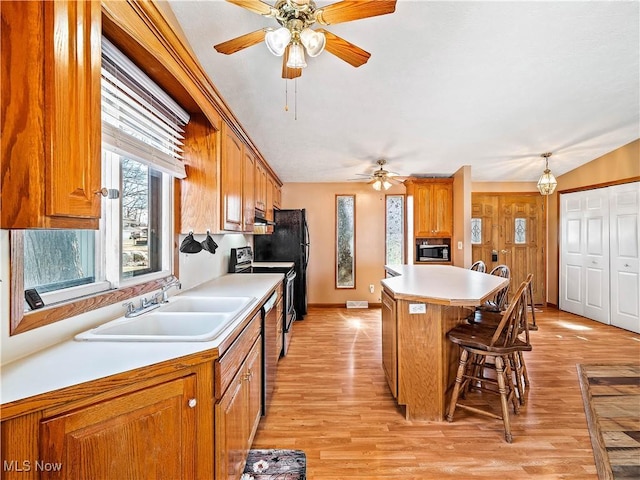 kitchen with light wood-style flooring, a sink, appliances with stainless steel finishes, a breakfast bar area, and light countertops