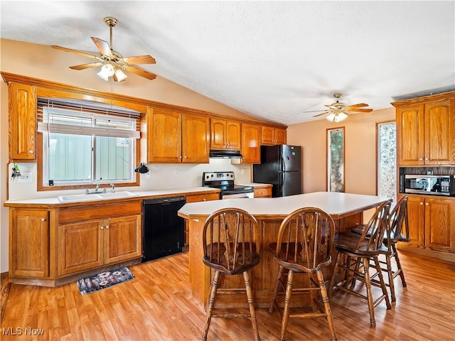 kitchen with a breakfast bar area, brown cabinetry, a sink, black appliances, and light wood-style floors