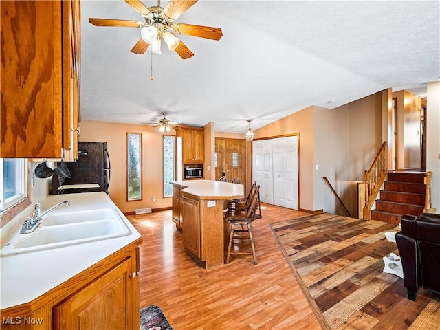 kitchen featuring stainless steel microwave, light wood-type flooring, light countertops, vaulted ceiling, and a kitchen breakfast bar