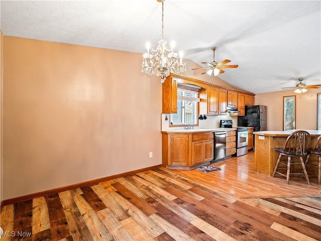 kitchen with brown cabinetry, light wood finished floors, stainless steel appliances, light countertops, and a kitchen bar