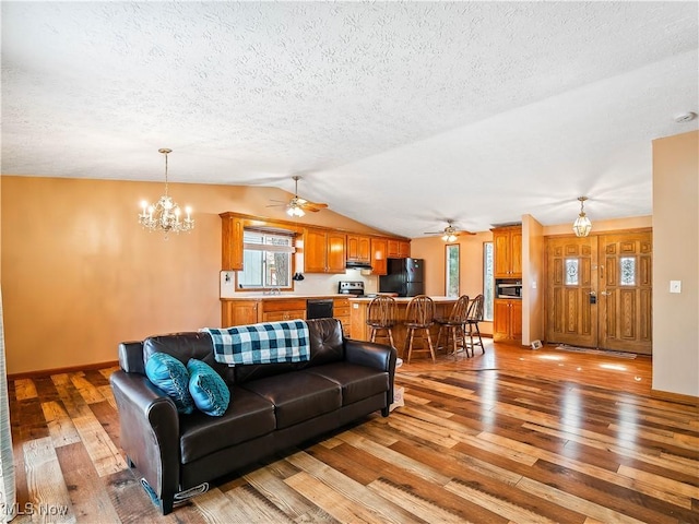 living room featuring ceiling fan with notable chandelier, a textured ceiling, vaulted ceiling, and light wood finished floors