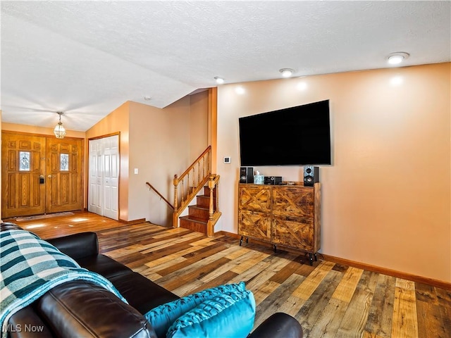 living area featuring a textured ceiling, stairway, baseboards, wood-type flooring, and lofted ceiling