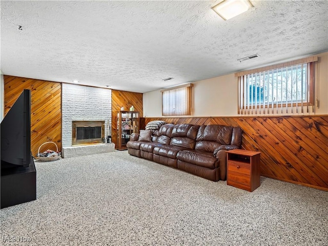 living room featuring wooden walls, visible vents, a brick fireplace, carpet floors, and a textured ceiling