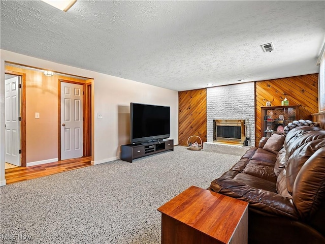 living room with visible vents, wood walls, carpet floors, a fireplace, and a textured ceiling