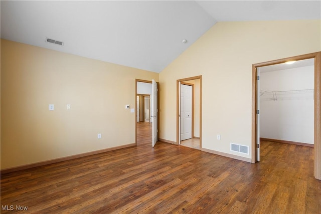 unfurnished bedroom featuring vaulted ceiling, visible vents, a spacious closet, and wood finished floors