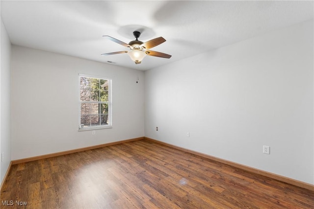 spare room with a ceiling fan, visible vents, wood finished floors, and baseboards