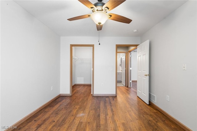 unfurnished bedroom with a spacious closet, visible vents, baseboards, wood finished floors, and a closet