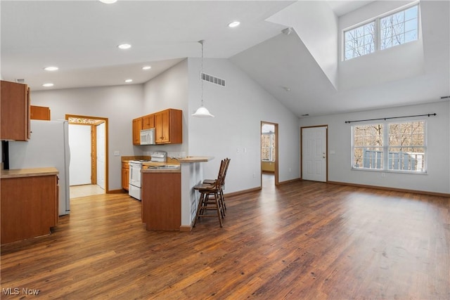 kitchen featuring a kitchen bar, dark wood-type flooring, open floor plan, white appliances, and brown cabinetry