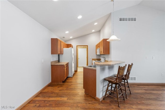 kitchen featuring visible vents, a breakfast bar, a peninsula, wood finished floors, and white appliances