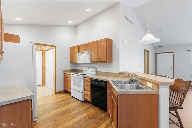 kitchen featuring visible vents, a breakfast bar, a sink, white appliances, and a peninsula