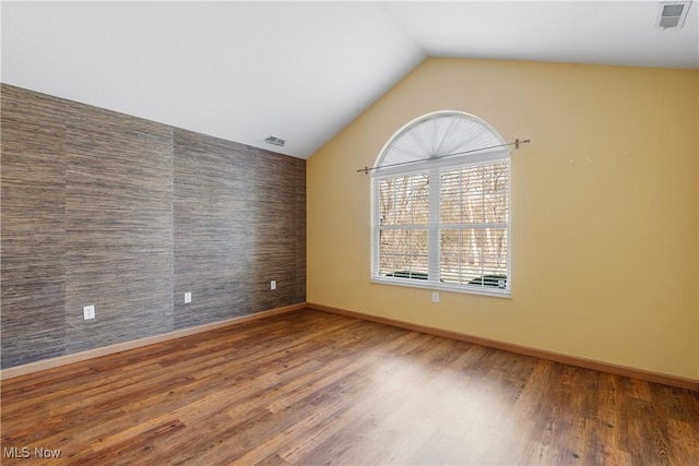 unfurnished room featuring visible vents, wood finished floors, baseboards, lofted ceiling, and an accent wall