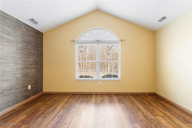 empty room with visible vents, an accent wall, and wood finished floors