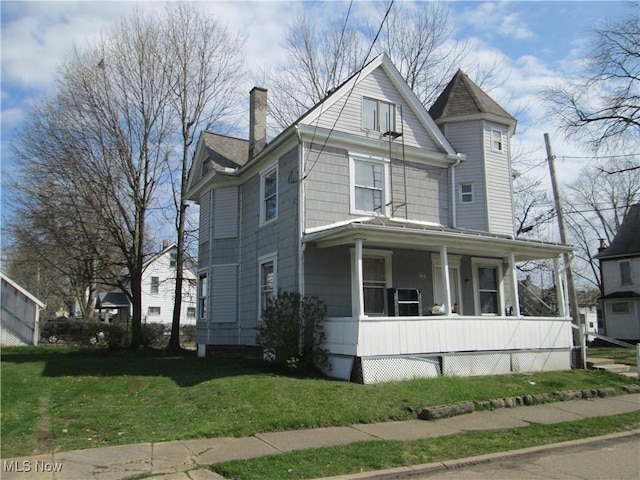 view of front of home featuring covered porch, a chimney, and a front yard