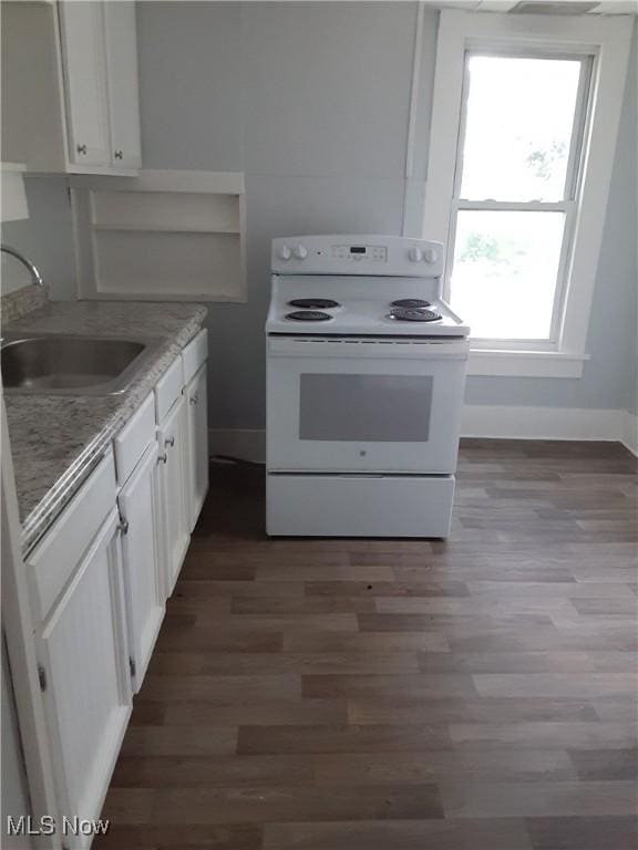 kitchen with white electric range oven, wood finished floors, baseboards, a sink, and white cabinets