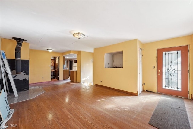 unfurnished living room featuring a wood stove, baseboards, and wood finished floors