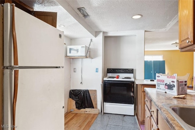 kitchen with a sink, white appliances, a textured ceiling, and light countertops