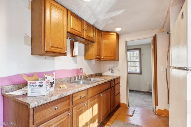 kitchen featuring a textured ceiling, brown cabinets, freestanding refrigerator, and a sink