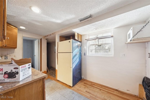 kitchen featuring light wood-type flooring, a textured ceiling, brown cabinetry, and freestanding refrigerator