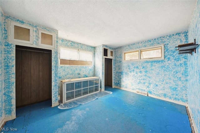 unfurnished living room with a textured ceiling, carpet flooring, and wallpapered walls