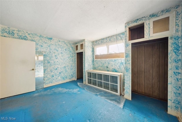 unfurnished living room featuring a textured ceiling and wallpapered walls