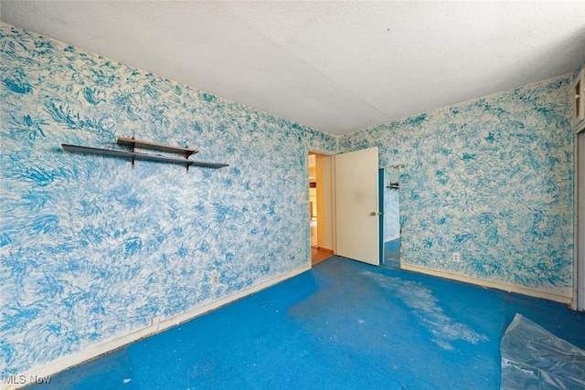 carpeted spare room featuring a textured ceiling, wallpapered walls, and baseboards