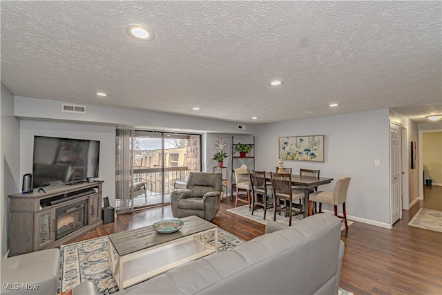 living area with visible vents, baseboards, recessed lighting, wood finished floors, and a glass covered fireplace