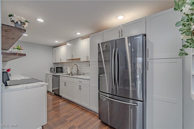 kitchen featuring a sink, backsplash, appliances with stainless steel finishes, light countertops, and dark wood-style flooring