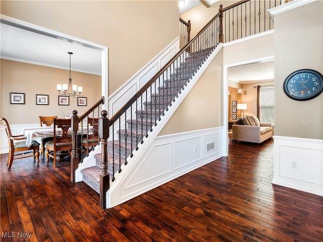 stairway with visible vents, ornamental molding, hardwood / wood-style flooring, wainscoting, and a chandelier