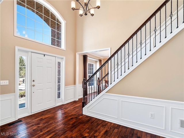 foyer featuring visible vents, dark wood-style floors, wainscoting, a chandelier, and stairs