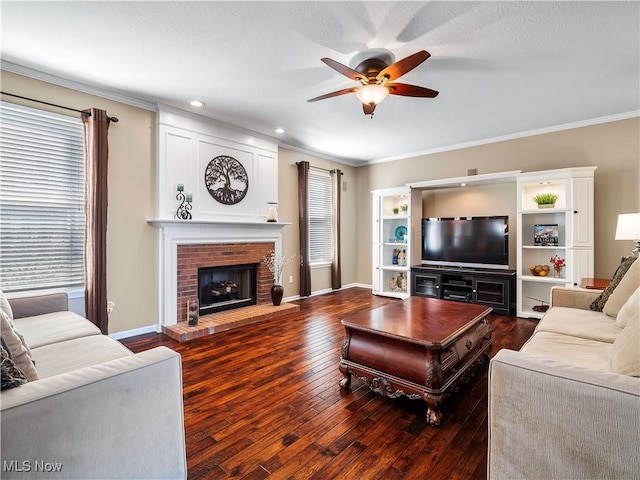 living room featuring a ceiling fan, baseboards, dark wood finished floors, crown molding, and a brick fireplace