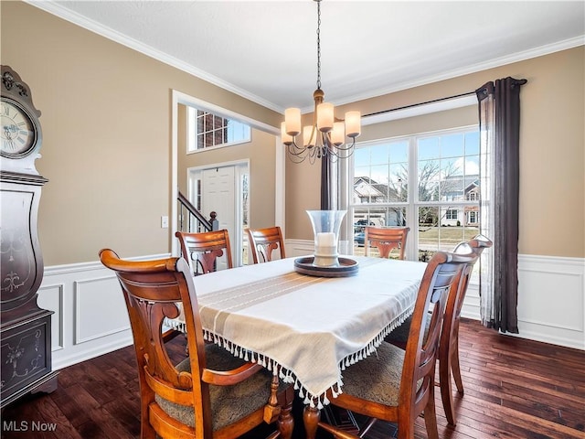 dining area featuring dark wood-type flooring, a notable chandelier, crown molding, and a wainscoted wall