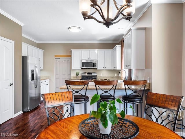 kitchen featuring dark wood finished floors, stainless steel appliances, a peninsula, crown molding, and a chandelier