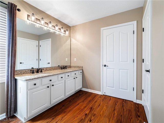 full bathroom featuring double vanity, baseboards, wood finished floors, and a sink