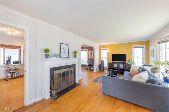 living room with arched walkways, light wood-style flooring, a tile fireplace, and crown molding