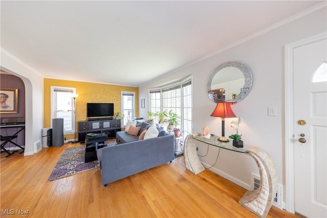 living area with light wood-type flooring, plenty of natural light, arched walkways, and baseboards