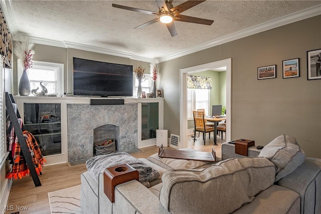 living room featuring ornamental molding, a fireplace, wood finished floors, a textured ceiling, and a ceiling fan