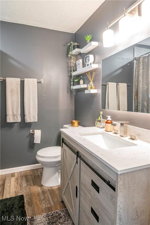 bathroom featuring baseboards, toilet, vanity, wood finished floors, and a textured ceiling