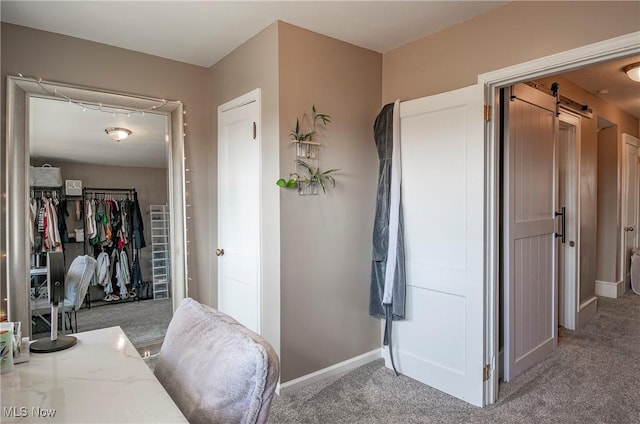 hall featuring a barn door, baseboards, and light carpet