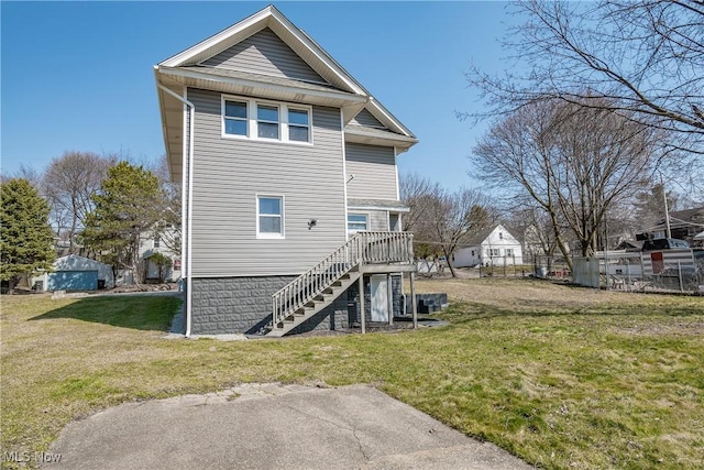 rear view of house with stairway, a yard, and fence