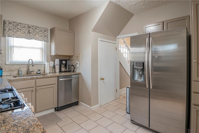 kitchen featuring a sink, backsplash, a textured ceiling, stainless steel appliances, and light tile patterned floors