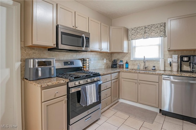 kitchen with a sink, decorative backsplash, appliances with stainless steel finishes, and light tile patterned flooring