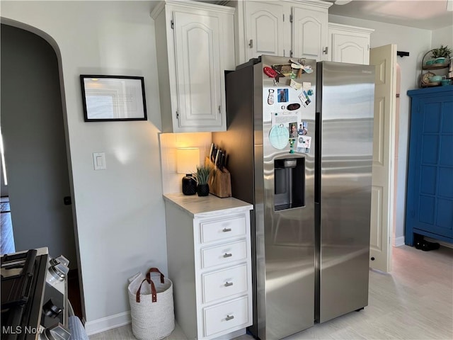 kitchen featuring tasteful backsplash, light countertops, stainless steel refrigerator with ice dispenser, arched walkways, and white cabinetry