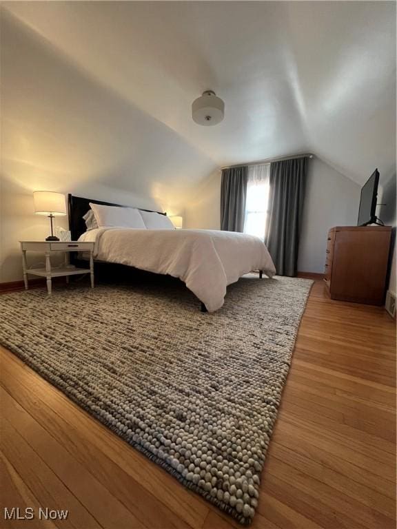 bedroom with vaulted ceiling, wood finished floors, and baseboards