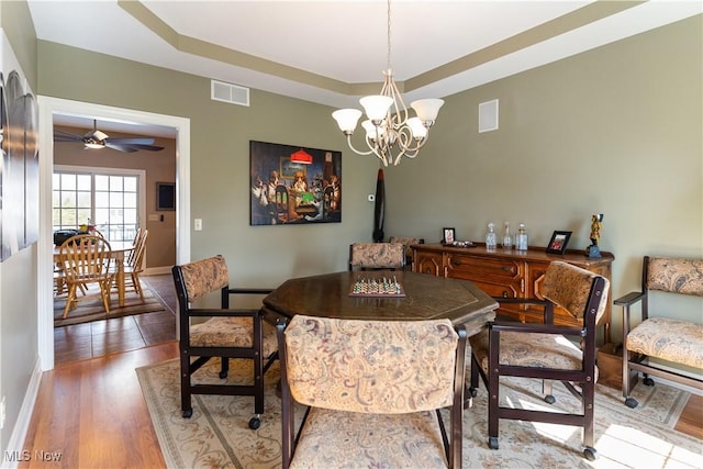 dining area with ceiling fan with notable chandelier, a tray ceiling, wood finished floors, and visible vents