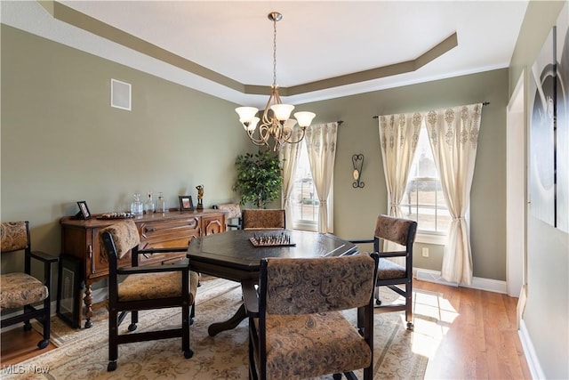 dining area with a notable chandelier, light wood-style flooring, baseboards, and a tray ceiling