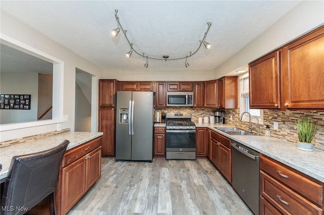 kitchen featuring a sink, tasteful backsplash, stainless steel appliances, brown cabinetry, and light wood finished floors