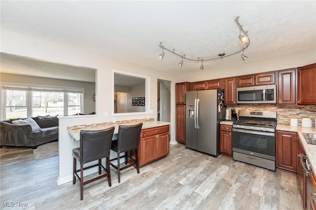 kitchen with light countertops, decorative backsplash, light wood-style flooring, a kitchen breakfast bar, and stainless steel appliances